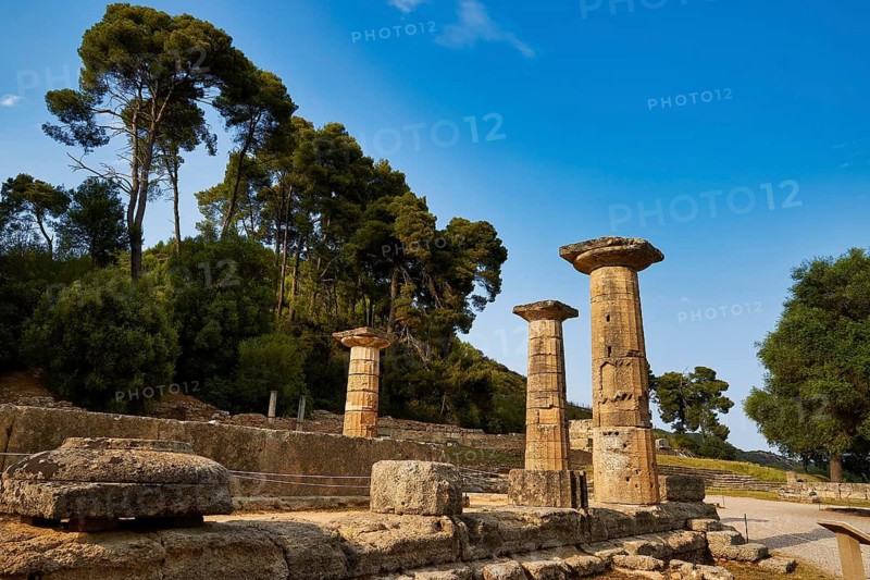 Hera Temple, Heraion, stone pillars against a background of tall trees and bright blue sky, Archaeological Site, Ancient Olympia, Olympia, Peloponnese, Greece