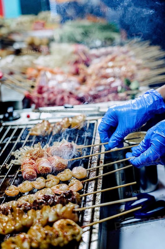 Close-up of a cropped unrecognizable food vendor preparing assorted meats on skewers at a bustling night market in Hong Kong, highlighting the city's vibrant street food scene