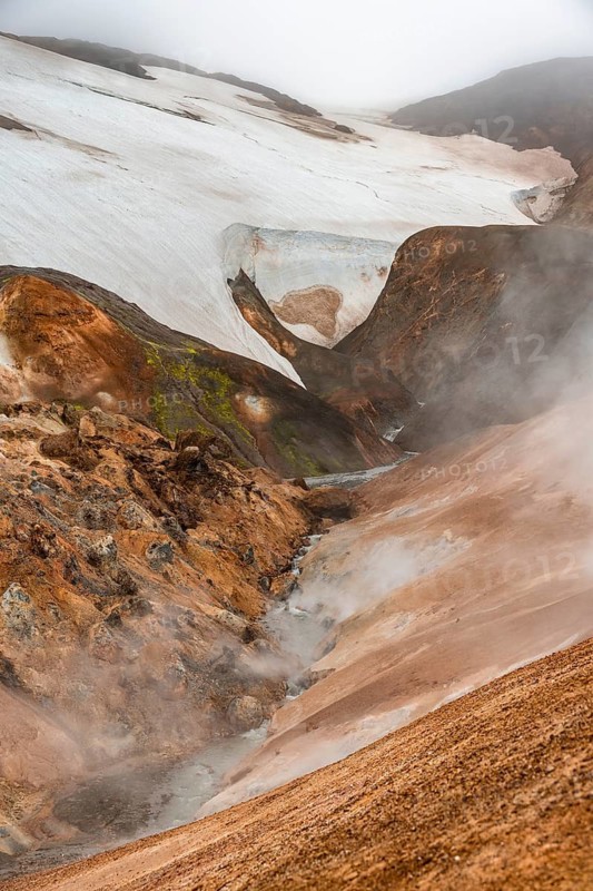 Steaming stream between colourful rhyolite mountains and snowfields, Hveradalir geothermal area, Kerlingarfjöll, Icelandic Highlands, Iceland