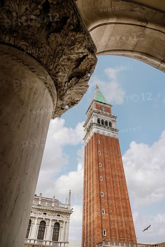 A stunning perspective of St. Mark's Campanile in Venice, framed by an ornate stone archway. The striking architecture captures the essence of Venetian charm and history