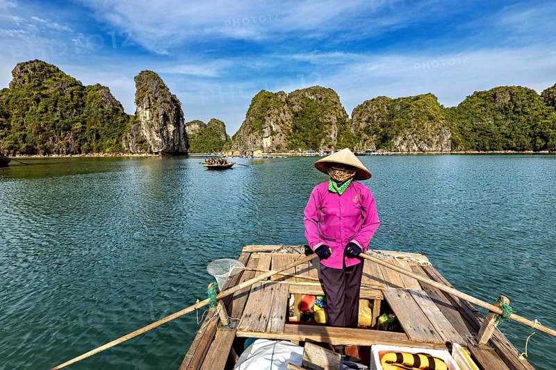 Fishermen on a boat in a picturesque bay with limestone cliffs, rowing boats for tourists in Halong Bay in Vietnam