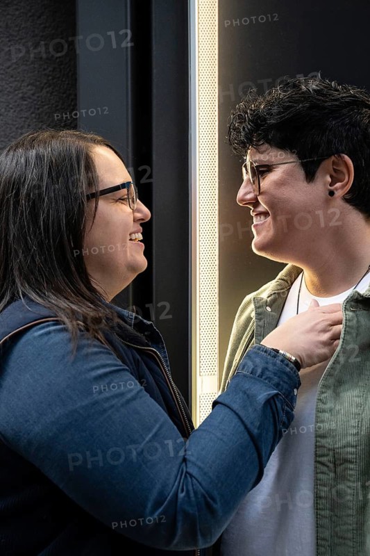 A lesbian couple joyfully smiling at each other, showcasing affection and connection. Their expressions reflect love and happiness in a candid and heartwarming moment