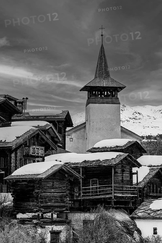 Old wooden houses with snow-covered roofs and the Saint Theodule church in the historic village centre, black and white photograph, Grimentz, Val d'Anniviers, Valais Alps, Canton Valais, Switzerland