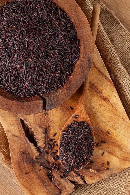 Natural black rice in a wooden bowl and spoon on a wooden surface in rustic style, top view