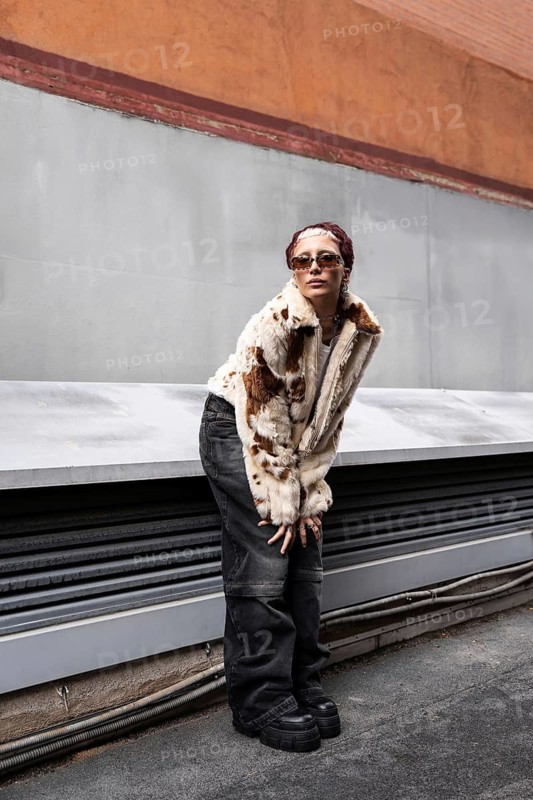 Stylish woman poses against an urban backdrop, showcasing a faux fur jacket, wide pants, and sunglasses. The scene embodies contemporary street fashion vibes