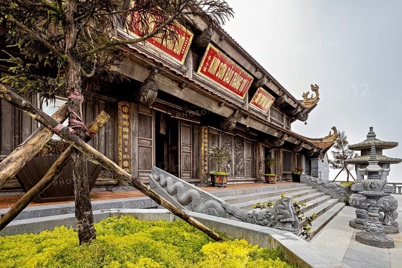 Traditional temple with wooden façade, surrounded by stone sculptures and plants, The temple complex at Fansipan near Sa Pa in Vietnam
