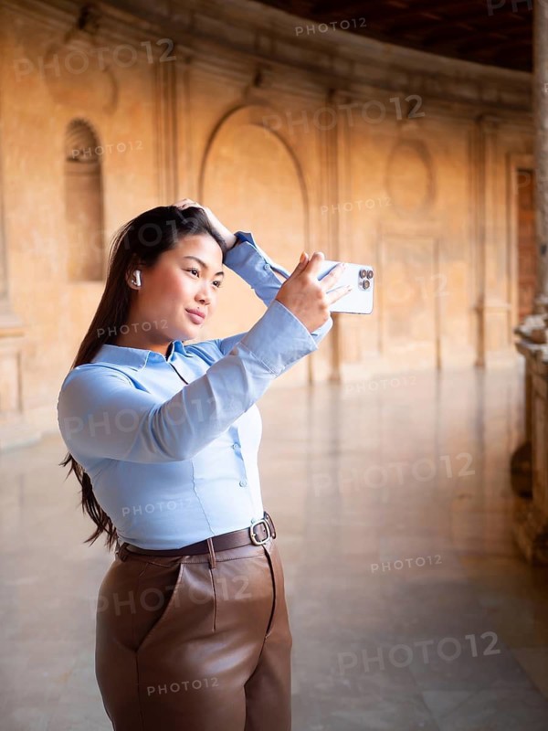 A woman is captured taking a selfie inside an ornate, historic building, showing a blend of modern technology and classic architecture