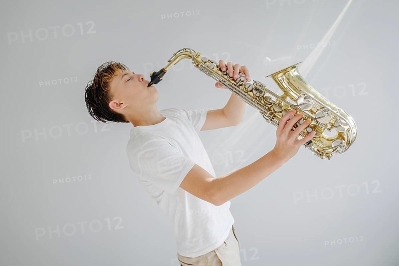 A young musician passionately playing a saxophone, dressed in a white shirt against a simple background. The image captures the essence of musical dedication and artistry