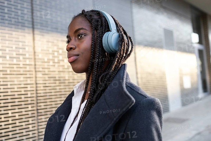 African American businesswoman with braids takes a break outdoors, wearing headphones and looking contemplative