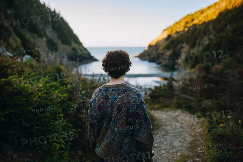 Back view of an unrecognizable woman contemplating the tranquil coastal scenery in Shoe Cove Beach, surrounded by lush greenery during sunset