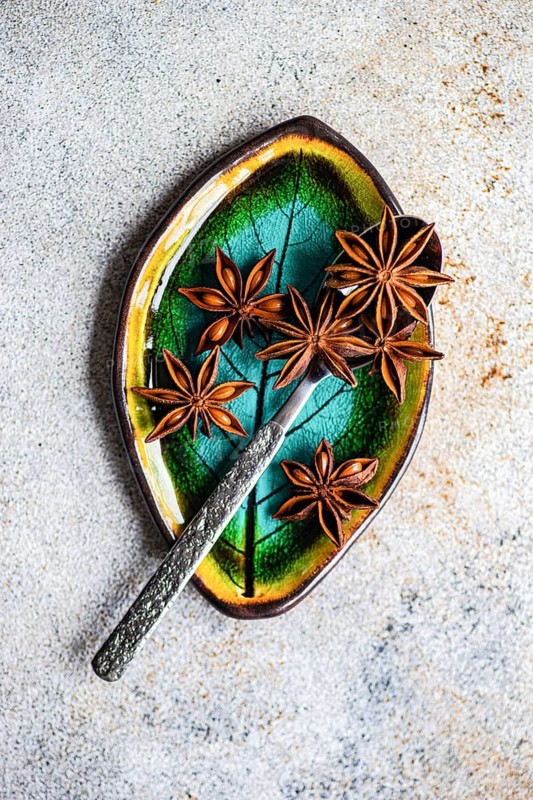 Top view of star anise beautifully arranged on a ceramic dish with vibrant green and yellow tones with spoon, resting on a textured grey surface