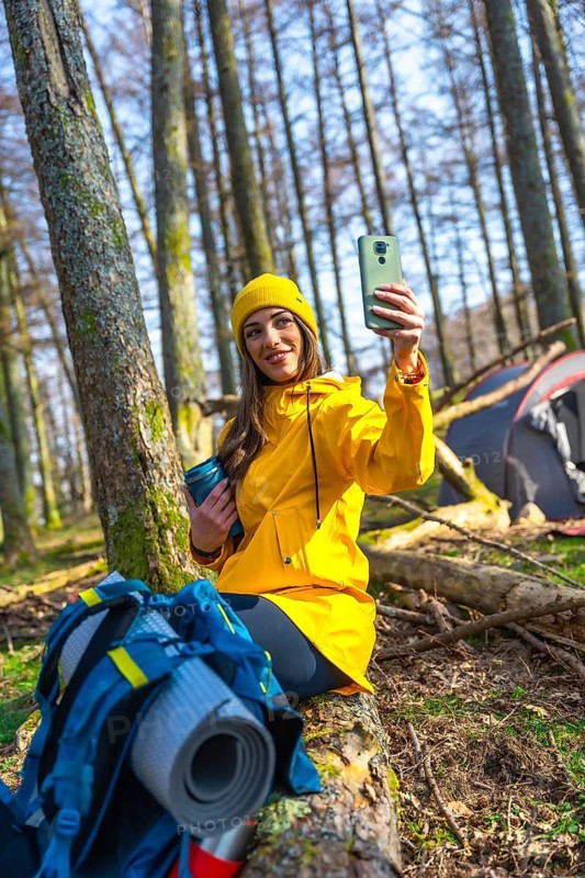 Young woman enjoying a joyful moment while taking a selfie in a serene forest during a camping adventure, surrounded by nature's beauty