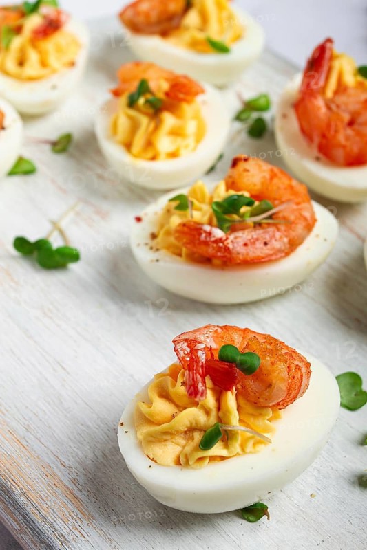 Boiled eggs stuffed with yolk and seasoned with mayonnaise, stuffed eggs with shrimp, on a white wooden chopping board, selective focus, close-up, without people