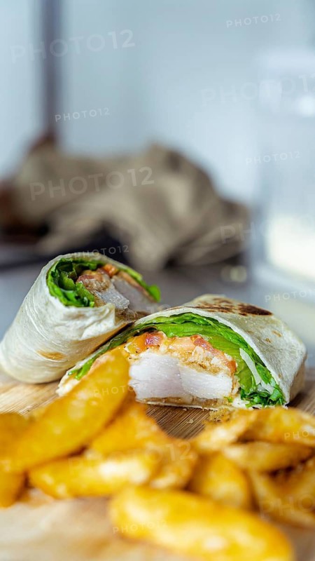 A close-up of a mouthwatering chicken wrap, filled with fresh lettuce and tomato, accompanied by crispy potato wedges on a wooden board. A perfect cafe meal scene