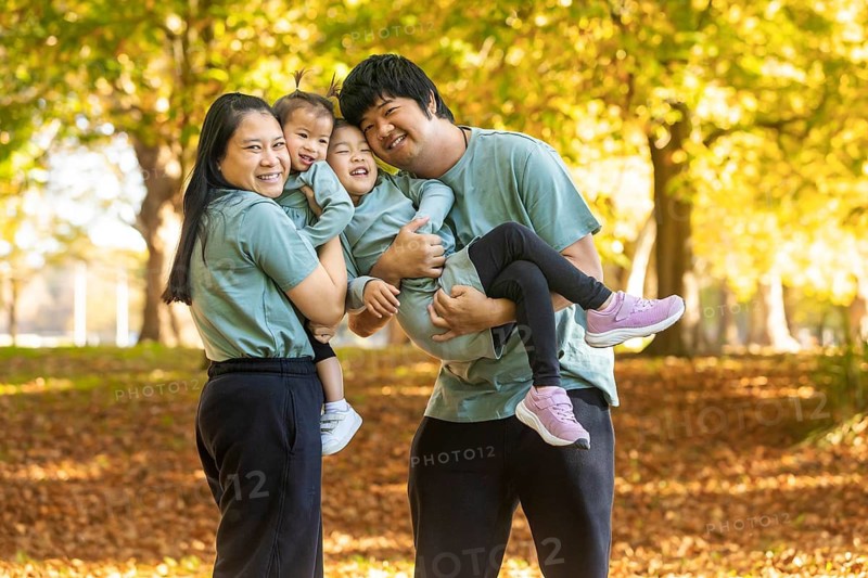 A joyful Asian family enjoying a sunny autumn day in a park. Smiling parents and children dressed in casual clothes pose together amidst the vibrant fall foliage for a picture