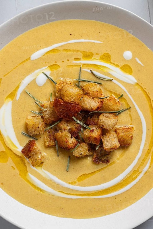 A creamy cauliflower curry soup topped with crunchy croutons and rosemary, styled on a white ceramic bowl Perfect for a healthy, homemade meal Close-up view