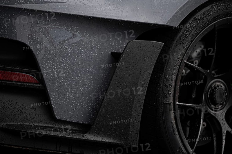 A close-up image focusing on the detailed elements of a wet sports car, showcasing its sleek design and racing features under dramatic lighting conditions
