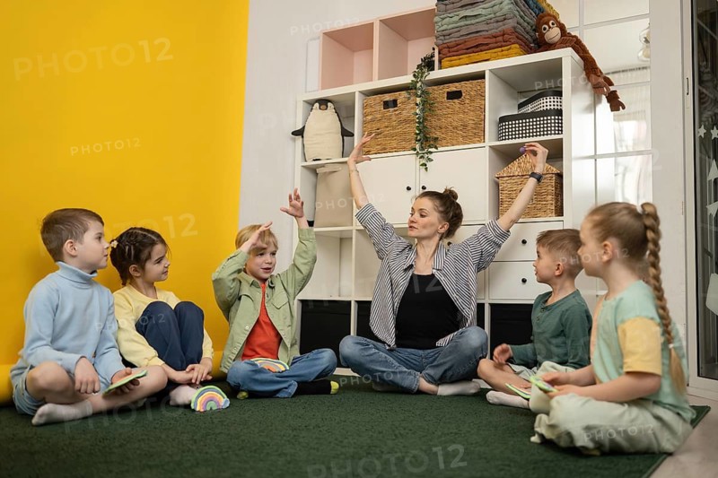 A teacher guides young children in a creative classroom activity, fostering imagination and teamwork. Bright room, toys, and shelves create an engaging learning environment