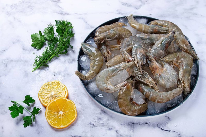 Fresh raw shrimp, spread on ice with lemon and cilantro slices on a marble surface, ready to cook, no people