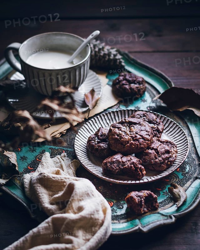 Rustic setting showcasing delicious chestnut cookies on a decorative plate with a steaming cup of milk. A warm, cozy atmosphere with autumn leaves and fabric accents