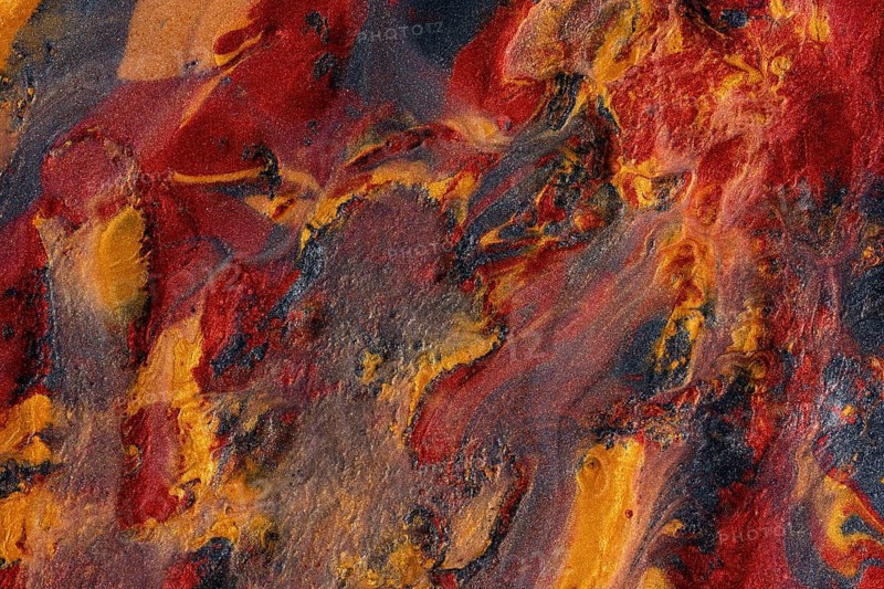 Close-up of an abstract, swirling texture combining metallic paints in vivid shades of red, gold, and dark colors for artistic and design backgrounds