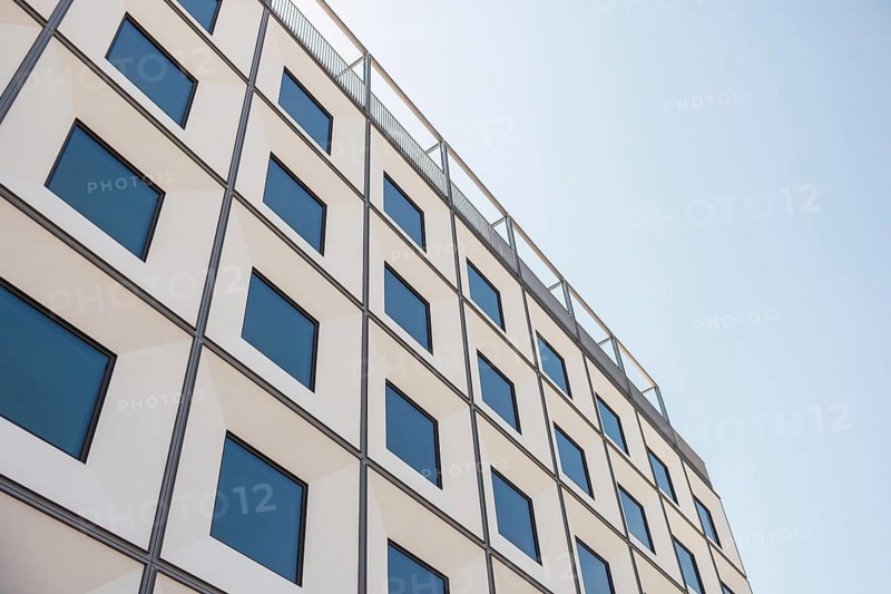 A modern building facade featuring geometric patterns and reflective windows under a clear blue sky. The symmetrical design highlights contemporary architectural style and urban aesthetics