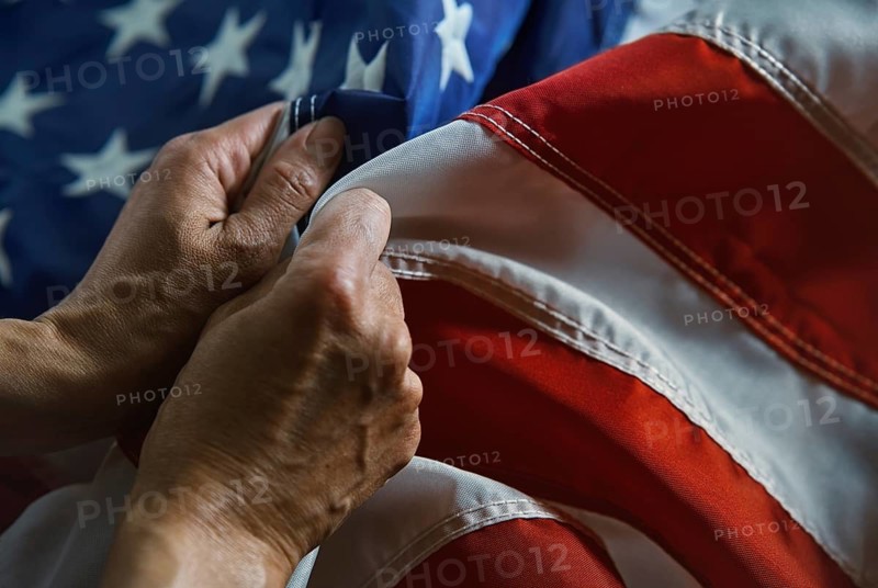 A close-up image showcases hands gently grasping the fabric of an American flag, emphasizing the details of the stars and stripes in a patriotic display