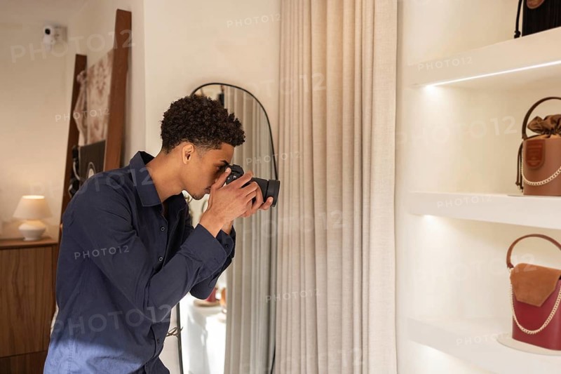 A skilled photographer focuses his camera on stylish luxury bags displayed elegantly on shelves in a modern store. The soft lighting accentuates the beautiful design