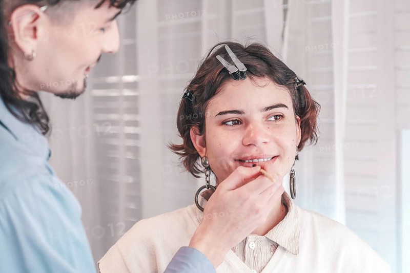 Professional makeup artist applying lip liner on a smiling model in a bright, modern beauty salon, highlighting diversity and preparation for a special event