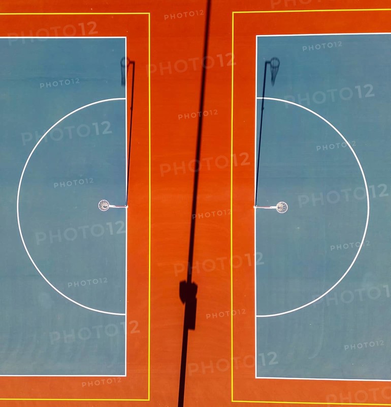 Top view captured by a drone of two netball courts. The aerial perspective highlights the geometric precision of the court lines and hoops, showcasing the layout and design typical of outdoor sports facilities
