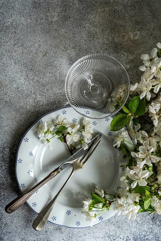 An elegant table setting featuring a vintage plate with a fork and knife, accompanied by delicate white flowers and a clear glass on a textured background