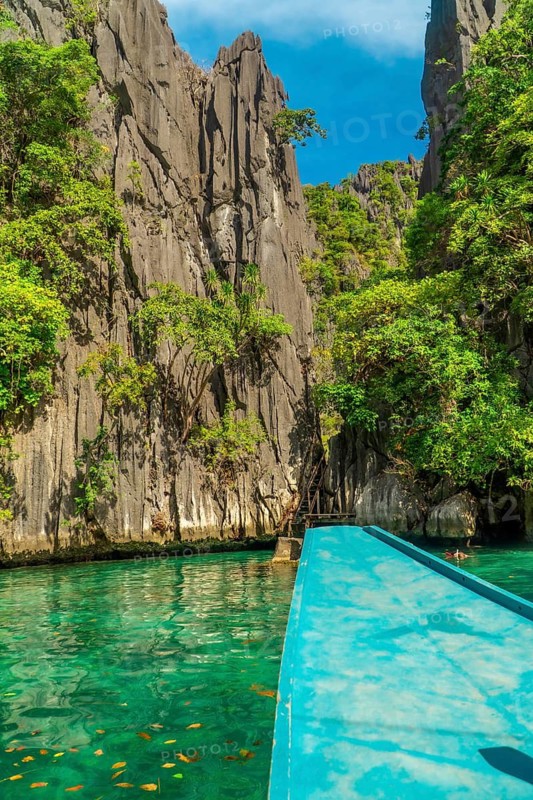 Traditional turquoise boat sailing on calm water between huge limestone cliffs in paradise twin lagoon, coron island, palawan, philippines