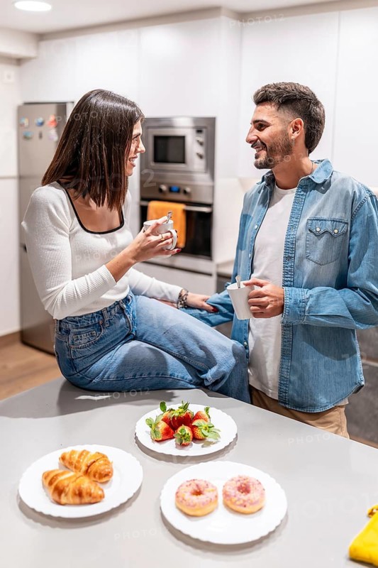 Young couple sharing a moment together, drinking coffee and enjoying a selection of pastries in their modern kitchen