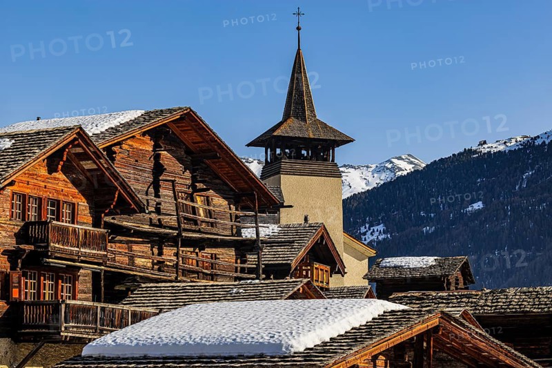 Snow-covered roofs of old farmhouses and barn storage, in the back the church tower of the Saint Theodule church, historic town center, Grimentz, Val d'Anniviers, Valais Alps, Canton of Valais, Switzerland