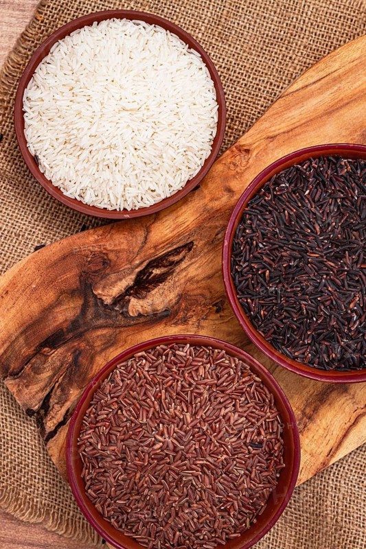 Set of red and black and white rice, in a bowl, on a wooden surface, rustic style, top view