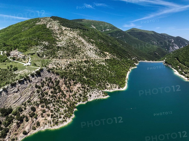 An aerial shot of Lago di Fiastra in Italy showcases its turquoise water bordered by lush green hills. The picturesque landscape highlights the serene and natural beauty of this breathtaking location
