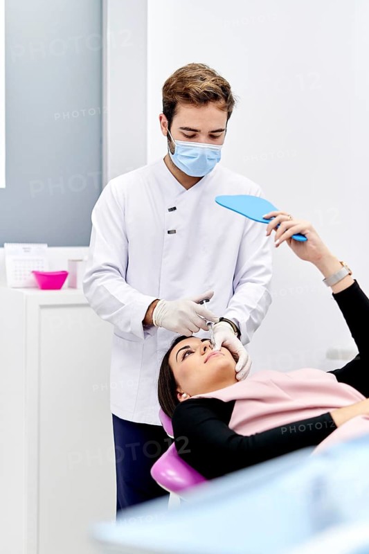 A doctor in a medical office administers a hyaluronic acid injection to a patient. The doctor wears a mask and sterile white gloves, ensuring a clean and safe procedure