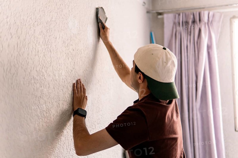 Unrecognizable man from behind plastering a white wall as part of a home remodeling project, focusing on wall preparation