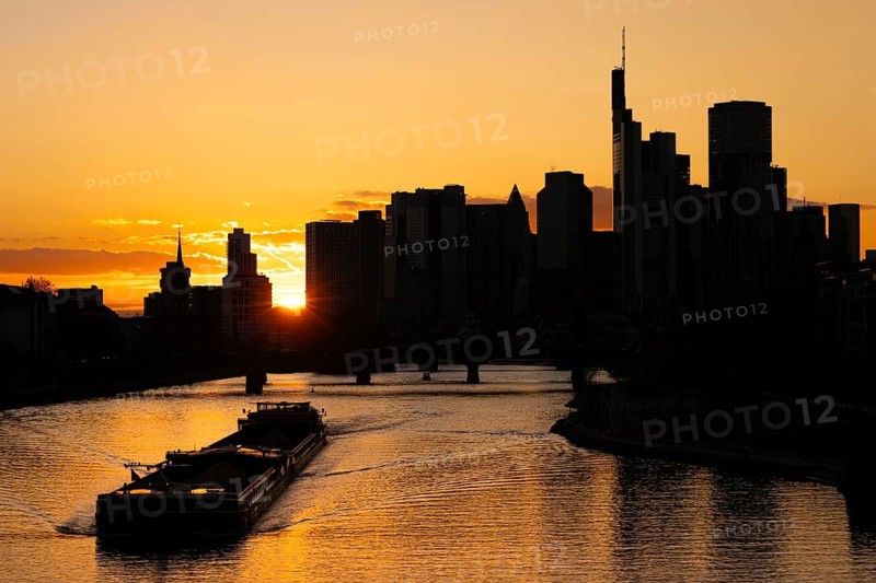 The sun sets behind the skyscrapers of Frankfurt's banking skyline as a barge sails along the Main, Frankfurt am Main, Hesse, Germany