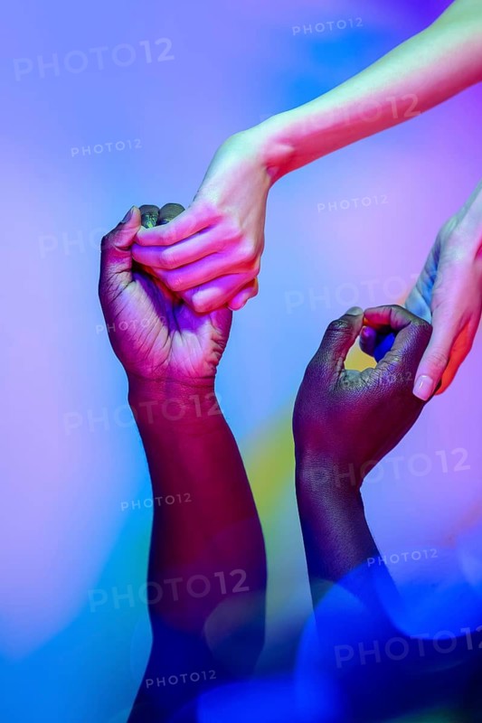 A diverse group of hands reaching out and connecting, illuminated by colorful lights, symbolizing unity and collaboration in a vibrant display of togetherness