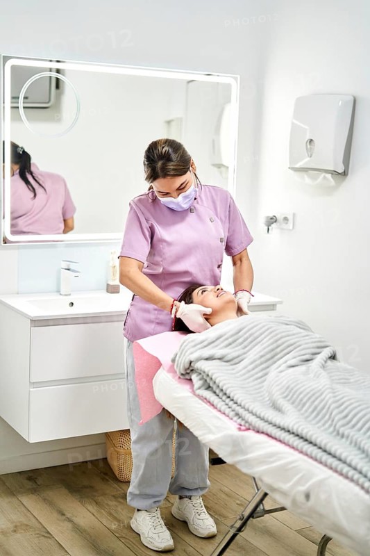 A skilled therapist provides a calming facial treatment to a client in a serene aesthetic medicine clinic. Soft lighting enhances the peaceful atmosphere during this rejuvenating session