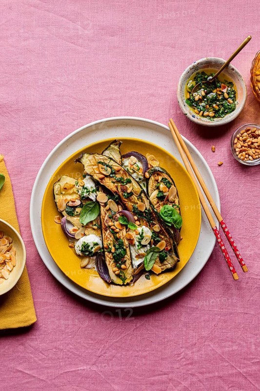 Top view of a colorful dish featuring roasted courgettes topped with mozzarella, basil, toasted almonds, and dressing, served on a vibrant yellow plate