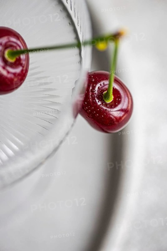 From above, a ripe cherry sits inside a textured glass, showcasing its vibrant red color and fresh appearance. The top view highlights the cherry's glossy texture