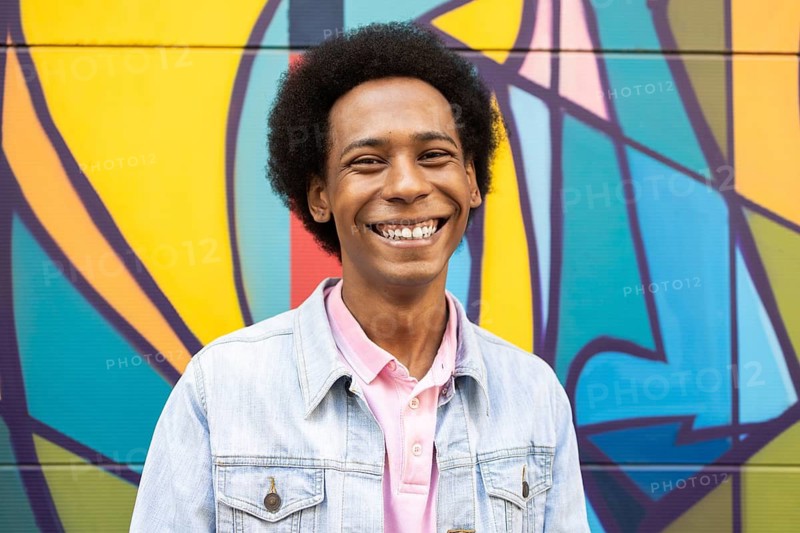 A joyful non-binary individual smiling brightly against a colorful mural backdrop. The vibrant colors and infectious smile capture a celebration of identity and positivity