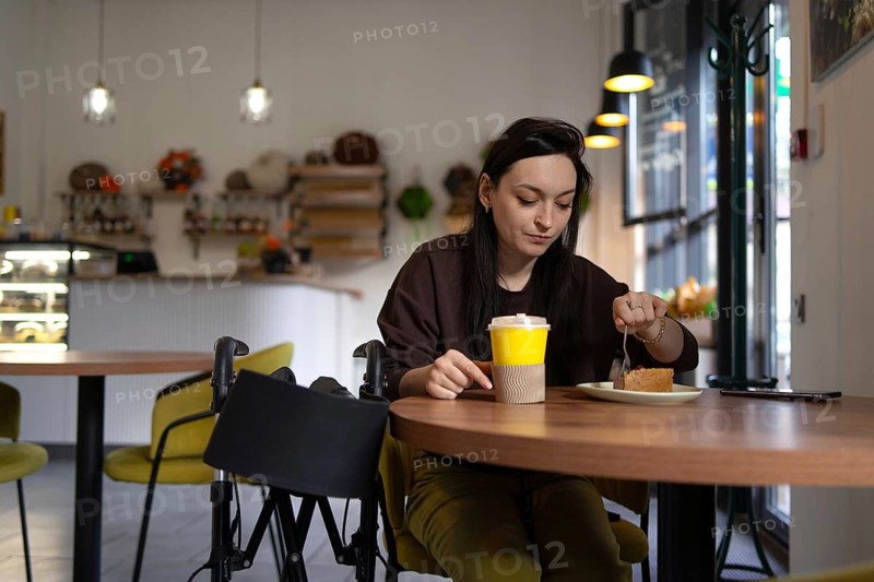 A woman with cerebral palsy enjoying coffee and cake at a cozy cafe. A relaxed ambiance with warm lighting and modern decor enhances her casual experience