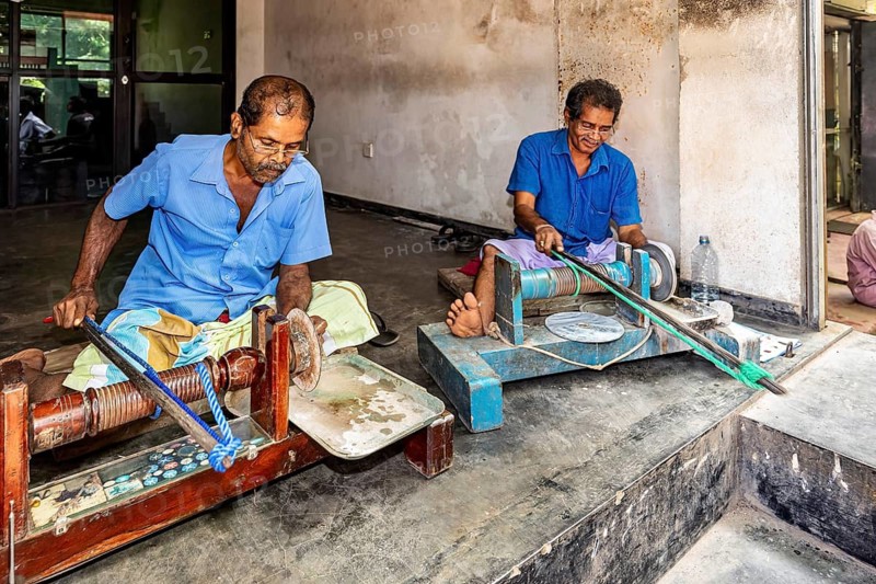 Two men in blue work clothes work on machines in parallel, the gemstone cutters in the city of Ratnapura in Sri Lanka
