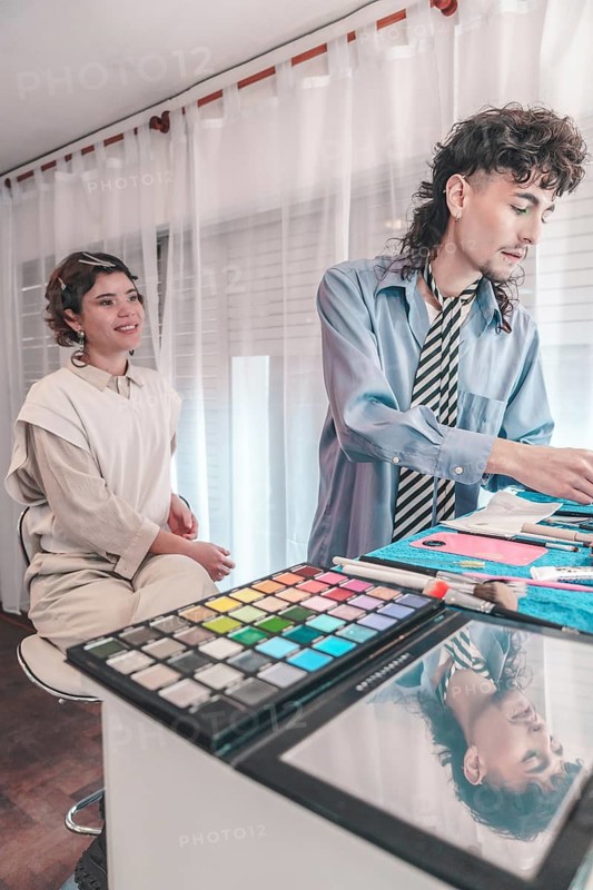 Professional makeup artist applying makeup on a model in a beauty salon, using a colorful eyeshadow palette and various brushes, showcasing diversity and inclusion in the beauty industry