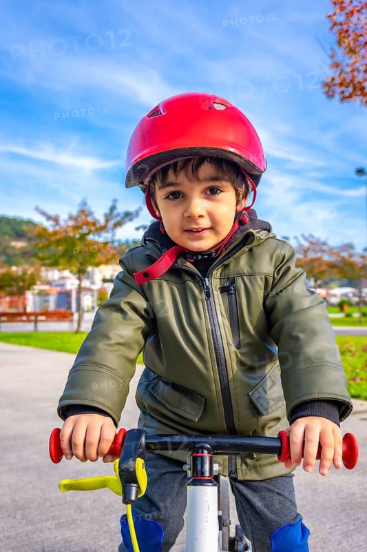 A young boy wearing a green jacket and a red helmet is riding a bike. The boy is smiling and he is enjoying himself