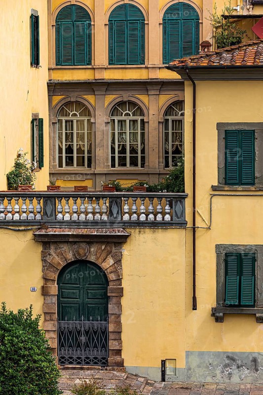 Arched entrance gate and arched windows with green shutters in a pastel-coloured façade, historic city centre, Lucca, Tuscany, Italy
