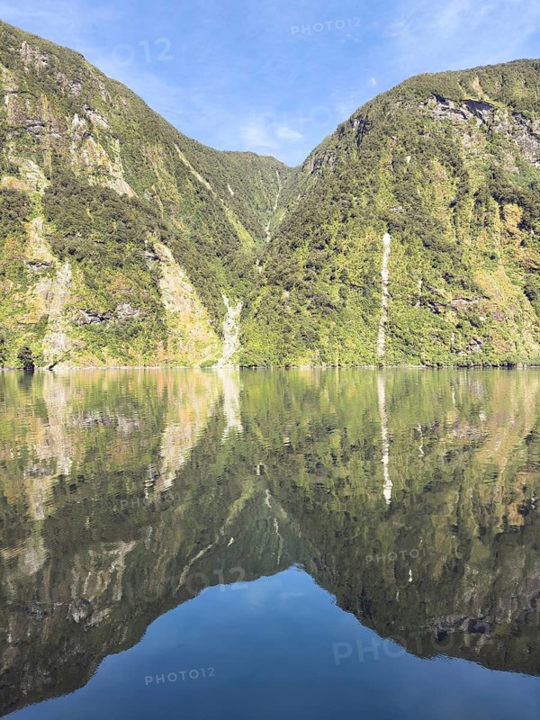 Mountains with reflections in the water against a blue sky in Doubtful Sound, South Island, New Zealand, Oceania